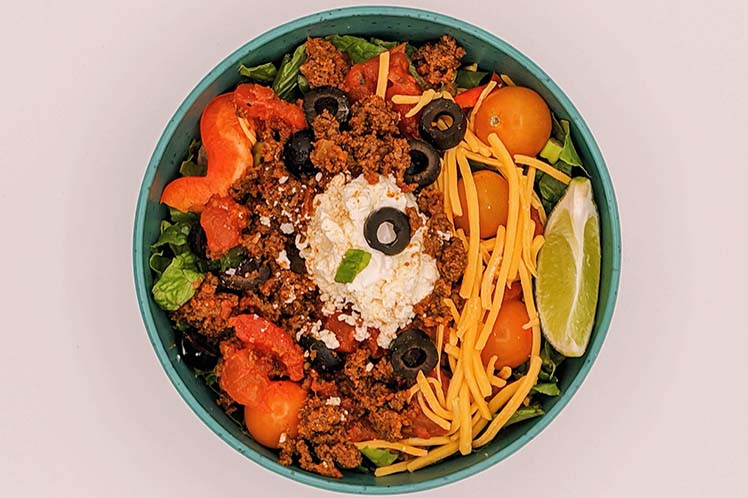 Taco bowl with seasoned ground beef and cheddar over mixed greens, with crispy tortilla strips