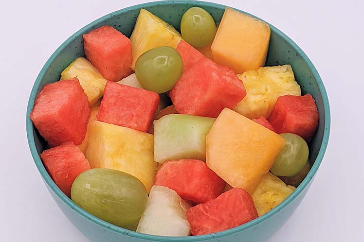 A bowl of seasonal fresh cut fruit salad with melon, grapes and berries.