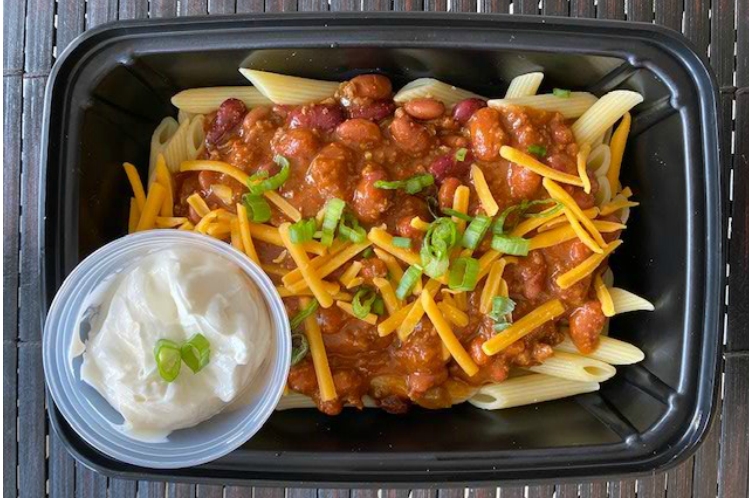 Chili mac bowl with chunky beef chili over pasta, topped with cheese, beans and diced onions
