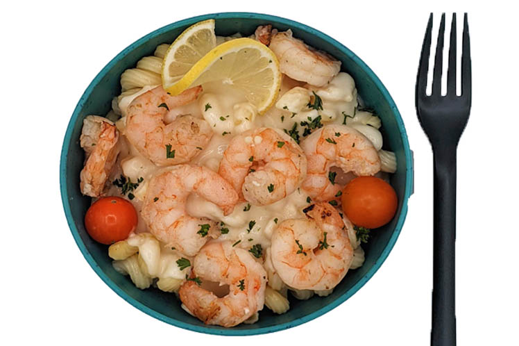 Bowl of grilled Gulf shrimp over pasta in creamy parmesan Alfredo sauce with cherry tomatoes.
