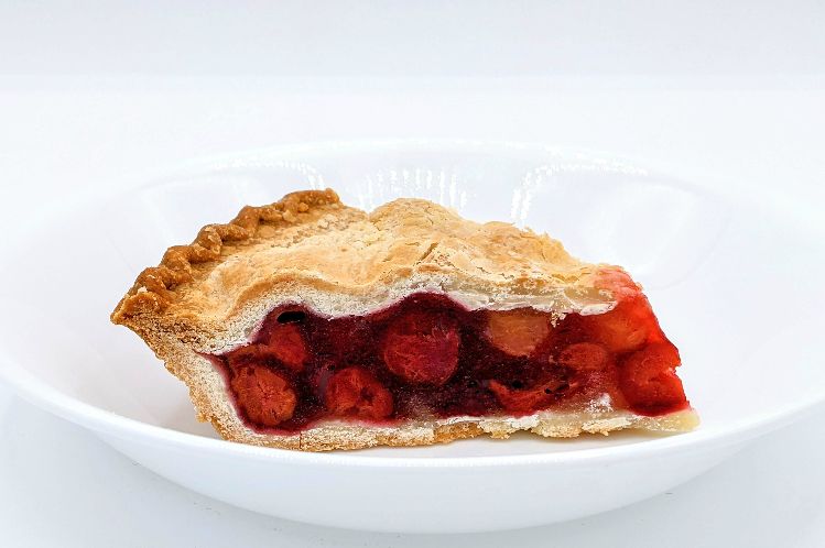 A slice of traditional cherry pie with fresh, plump cherries and a crisp golden crust.